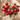 Bouquet of red and pink flowers in a white vase on a round stone surface with a beige wall background.